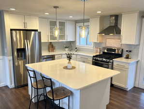 Kitchen featuring white cabinets, stainless steel appliances, wall chimney exhaust hood, glass insert cabinets, and pendant lighting
