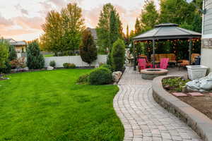 Summer view of yard at dusk with a gazebo, a patio area, a fenced backyard, and an outdoor living space with a fire pit