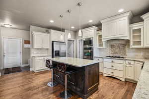 Kitchen featuring light stone counters, a breakfast bar area, backsplash, stainless steel appliances, and hanging light fixtures
