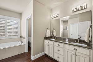 Bathroom featuring wood finish floors, plenty of natural light, double vanity, and a garden tub