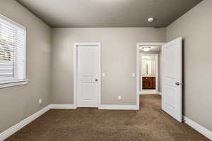 Unfurnished bedroom featuring dark colored carpet and baseboards