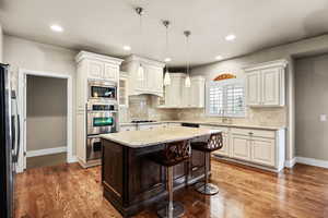 Kitchen featuring light stone counters, pendant lighting, a breakfast bar area, stainless steel appliances, and dark brown cabinets