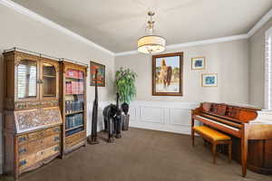 Living area featuring a wainscoted wall, a decorative wall, crown molding, and carpet flooring