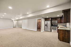 Kitchen with stainless steel appliances, open floor plan, dark brown cabinetry, carpet, and light stone counters