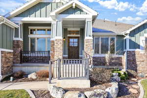 Property entrance with stone siding, board and batten siding, covered porch, and roof with shingles