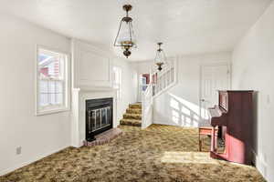 Unfurnished living room with carpet floors, a glass covered fireplace, stairway, and a textured ceiling