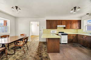 Kitchen featuring light countertops, white appliances, a peninsula, a textured ceiling, and under cabinet range hood