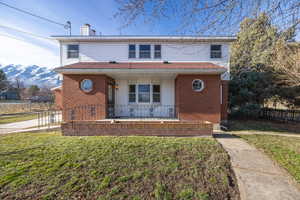 View of front of property with brick siding, covered porch, and a chimney