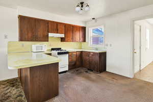 Kitchen with a peninsula, white appliances, light countertops, under cabinet range hood, and a breakfast bar area
