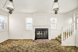 Unfurnished living room featuring a glass covered fireplace, carpet floors, and healthy amount of natural light