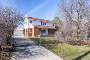 View of front of home with an outbuilding, concrete driveway, a chimney, brick siding, and a detached garage