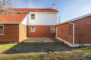 Back of house featuring a patio, a chimney, and brick siding