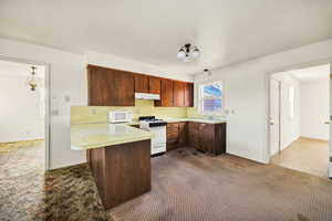 Kitchen featuring a peninsula, light countertops, white appliances, a breakfast bar, and dark carpet