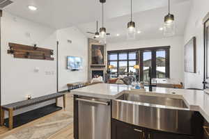 Kitchen with vaulted ceiling, light stone counters, light wood finished floors, stainless steel dishwasher, and a tile fireplace