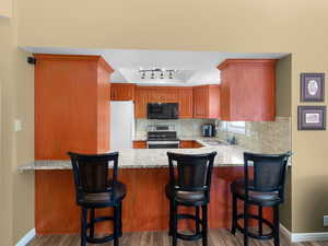 Kitchen with stainless steel electric range oven, light stone counters, backsplash, freestanding refrigerator, and black microwave