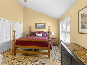 Bedroom with two closets, light wood-style flooring, a ceiling fan, and high vaulted ceiling