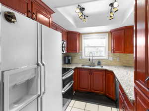 Kitchen with white refrigerator with ice dispenser, light stone countertops, range with two ovens, light tile patterned floors, and backsplash