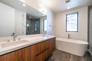 Full bathroom with a freestanding tub, double vanity, a stall shower, dark tile patterned flooring, and recessed lighting