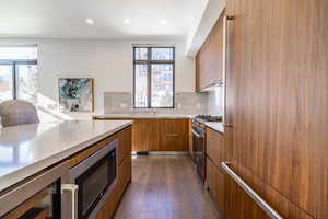 Kitchen with modern cabinets, built in microwave, dark wood-style floors, stainless steel range with gas cooktop, and backsplash