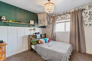Carpeted bedroom featuring a wainscoted wall, a decorative wall, a chandelier, and a textured ceiling