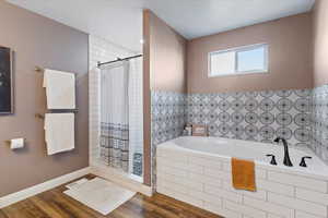 Full bath featuring a stall shower, a garden tub, and wood finished floors