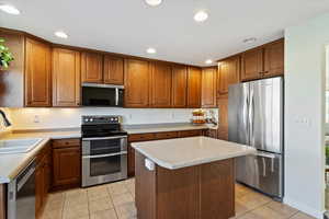 Kitchen featuring stainless steel appliances, brown cabinetry, light tile patterned floors, a center island, and light countertops