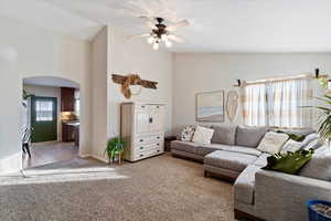 Living area with light colored carpet, arched walkways, ceiling fan, and high vaulted ceiling