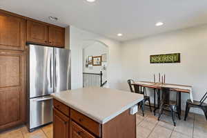 Kitchen with brown cabinets, freestanding refrigerator, a kitchen island, light countertops, and arched walkways