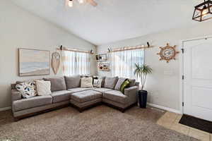 Living area featuring lofted ceiling, a textured ceiling, light tile patterned floors, light colored carpet, and a ceiling fan
