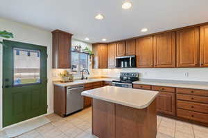 Kitchen featuring stainless steel appliances, brown cabinetry, light countertops, a kitchen island, and light tile patterned flooring