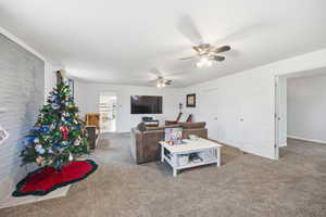 Living area with carpet, ceiling fan, and brick wall