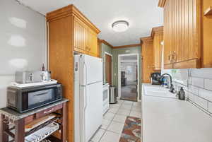 Kitchen featuring white appliances, brown cabinets, light countertops, light tile patterned flooring, and ornamental molding