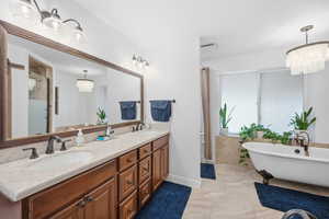Bathroom featuring a chandelier, a freestanding tub, double vanity, a stall shower, and light marble finish flooring