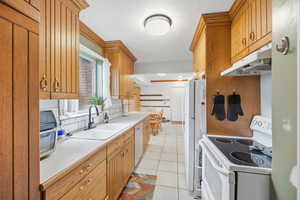 Kitchen with white appliances, light countertops, light tile patterned floors, under cabinet range hood, and brown cabinetry