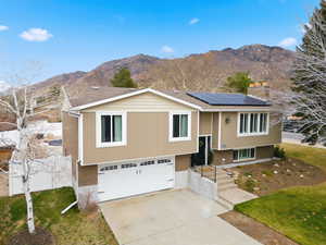 Bi-level home with brick siding, concrete driveway, roof mounted solar panels, a mountain view, and a garage