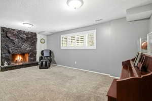 Living area with a textured ceiling, carpet floors, and a stone fireplace