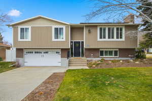 Bi-level home featuring concrete driveway, an attached garage, brick siding, and a chimney