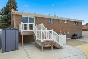 Back of property featuring a patio area, a shed, brick siding, stairway, and a chimney