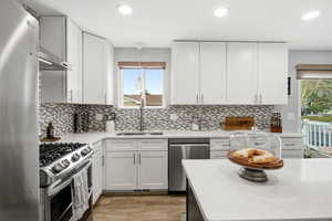 Kitchen with appliances with stainless steel finishes, white cabinetry, light stone countertops, recessed lighting, and light wood-type flooring