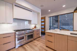 Kitchen with modern cabinets, double oven range, ventilation hood, white cabinetry, and light brown cabinets