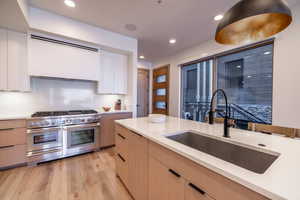 Kitchen with double oven range, modern cabinets, range hood, light brown cabinets, and light wood-style flooring