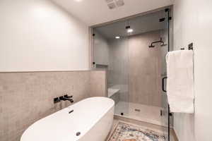 Bathroom featuring a freestanding bath, tile walls, a shower stall, recessed lighting, and a wainscoted wall