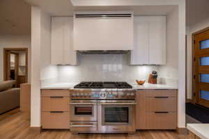 Kitchen with double oven range, range hood, modern cabinets, light wood-style flooring, and light brown cabinetry