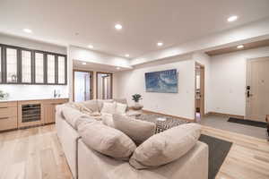 Living area featuring bar with sink, beverage cooler, light wood finished floors, and recessed lighting