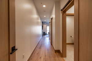 Hallway with a barn door, recessed lighting, and light wood-type flooring