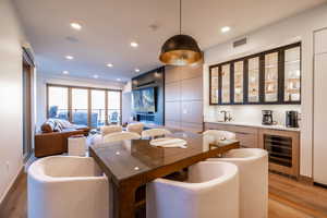 Dining room featuring wine cooler, light wood-type flooring, recessed lighting, bar with sink, and a tiled fireplace