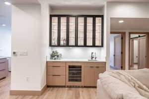 Indoor wet bar featuring a barn door, recessed lighting, glass insert cabinets, wine cooler, and light wood-style floors