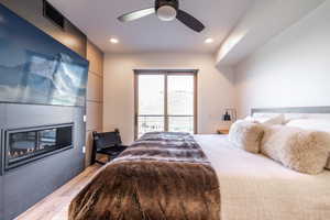 Bedroom with access to exterior, a glass covered fireplace, light wood-type flooring, ceiling fan, and recessed lighting