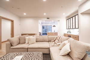 Living room with recessed lighting, bar with sink, and wood finished floors