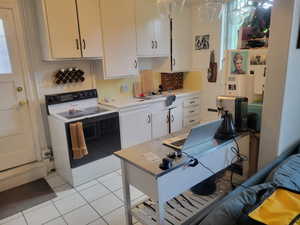 Kitchen with white range with electric cooktop, light countertops, white cabinetry, light tile patterned floors, and tasteful backsplash